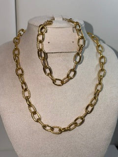 A chunky gold chain necklace displayed on a beige fabric mannequin bust, with a second, shorter gold chain draped behind it.