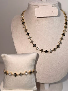 A gold and black floral bead necklace displayed on a cream jewelry bust, with a matching beaded bracelet resting on a small cream pillow.