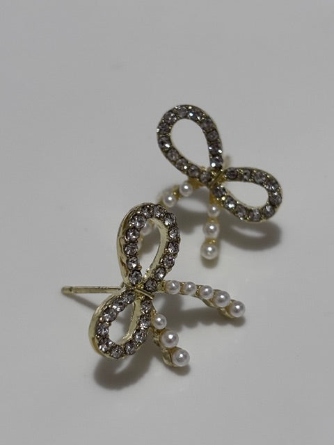 Bow-shaped earrings with pearl accents on a light gray background