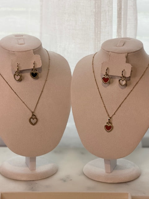 Two mannequin heads with necklaces with heart-shaped pendants and matching earrings on a neutral background.