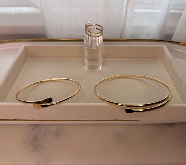 Set of gold bracelets on a white tray with a matching ring on a glass stand