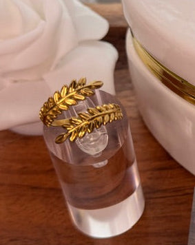 Gold ring with leaf design on a clear stand against a blurred background