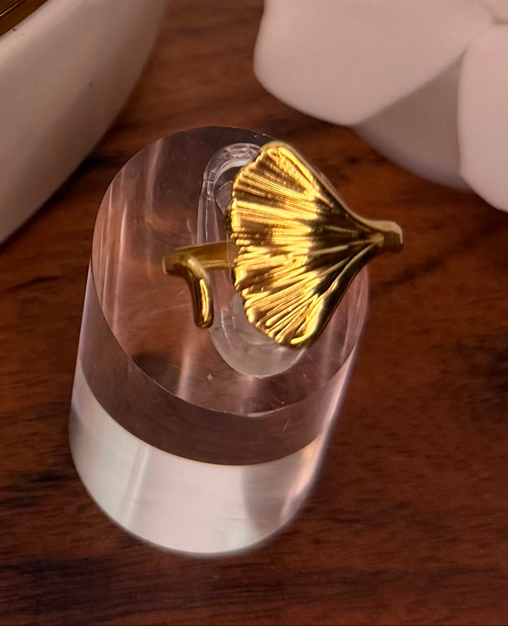 Gold leaf-shaped open ring on a clear stand against a wooden background
