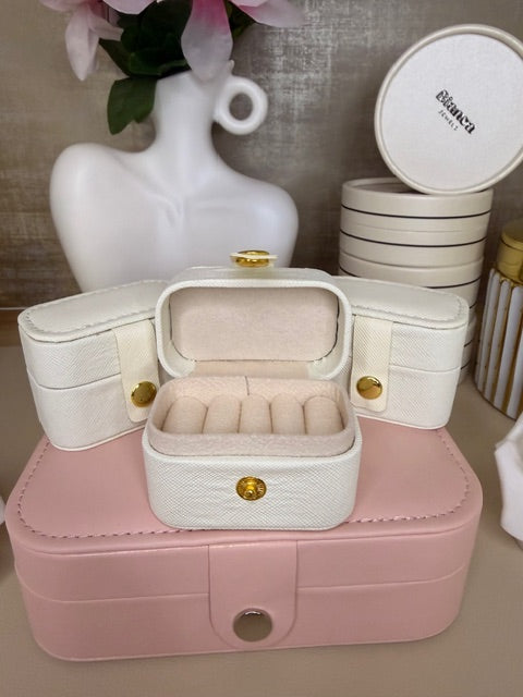 Pink jewelry box with and open ring jewelry box on top with flowers in the nbackground