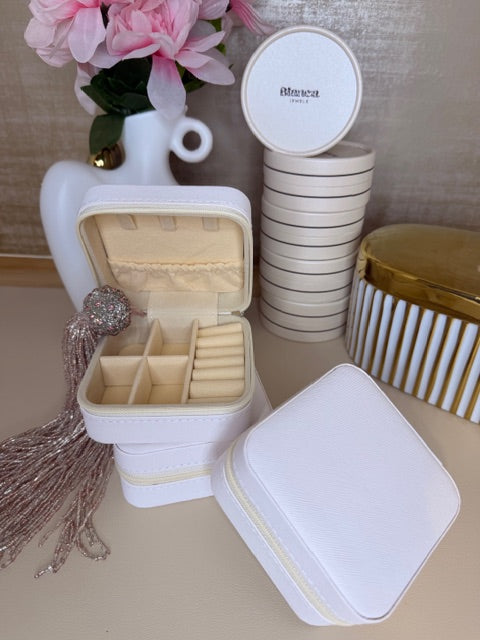 White jewelry box with gold accents, flowers, and a comb on a beige surface