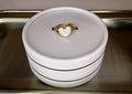 Gold ring with a heart-shaped stone in a white box on a metallic surface.