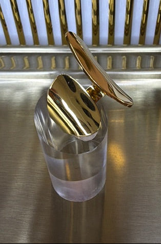 gold geometric open ring on a clear stand and on a metallic surface