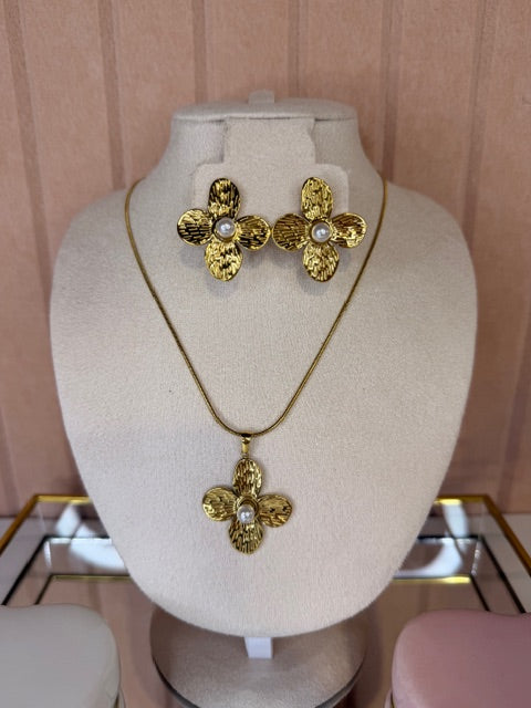 Gold earrings with floral design and matching necklace on a white bust against a pink background