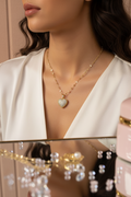 A close-up lifestyle shot of a woman wearing a delicate gold chain necklace with a heart-shaped pendant. The pendant is decorated with sparkling clear crystals and has a rose gold accent at the top.