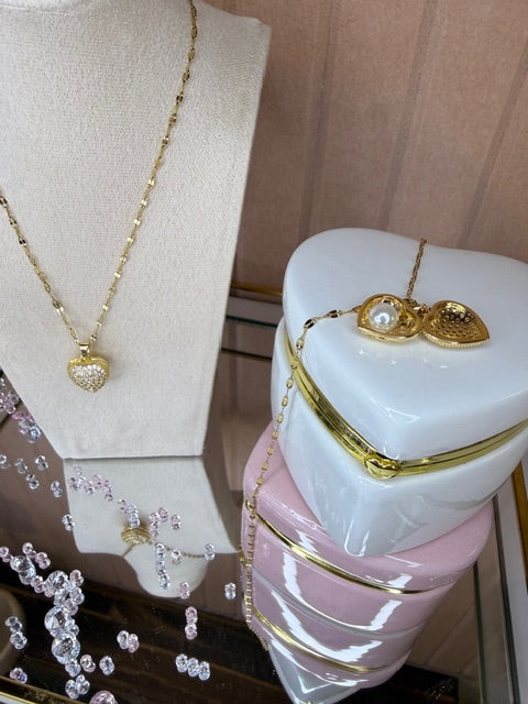Gold necklace on a white heart shaped trinket box with a bust and a necklace in the background