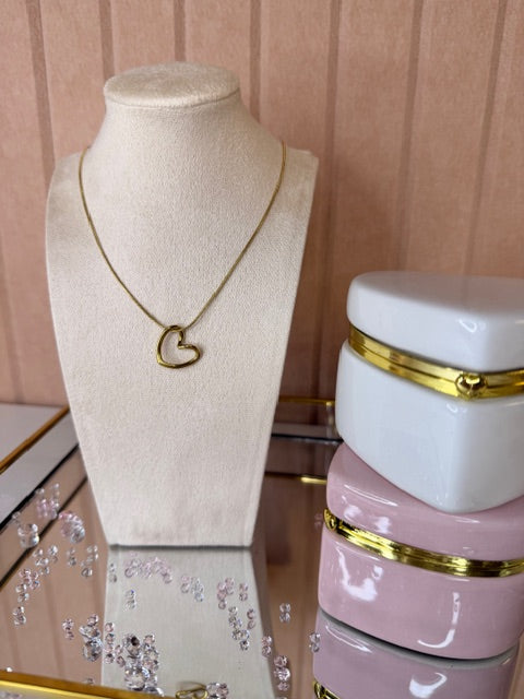Gold necklace on a beige display stand with pink and gold jewelry in the background.