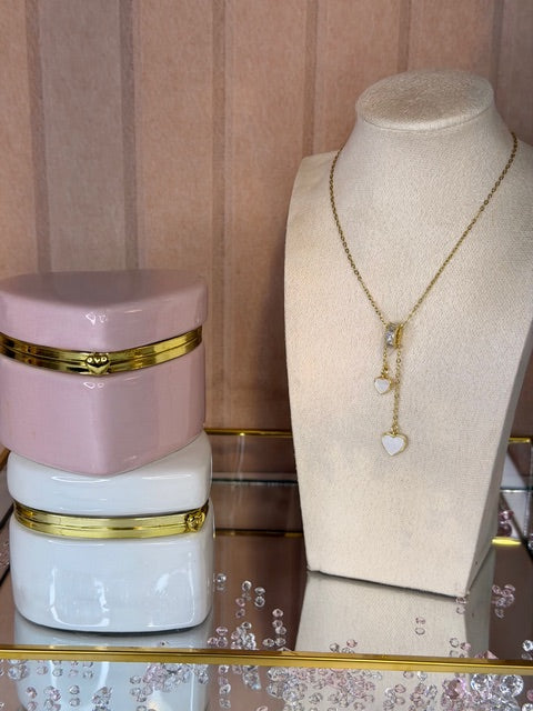 Gold necklace with two white heart shaped dangling pendants on a mannequin bust with decorative pink and white vases below.
