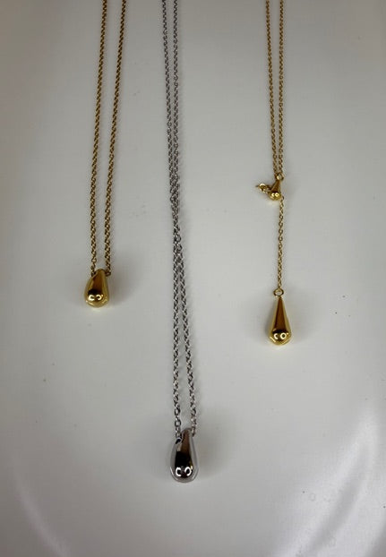 Three gold and silver necklaces with teardrop pendants on a white surface.