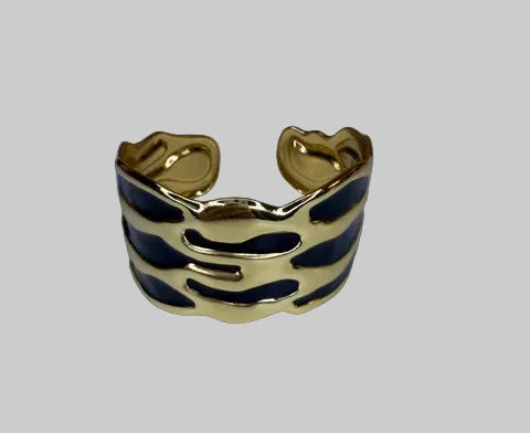 Gold and black oil drip design cuff bracelet on a light gray background
