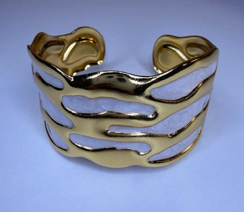 Gold bracelet with white oil drip design on a light blue background