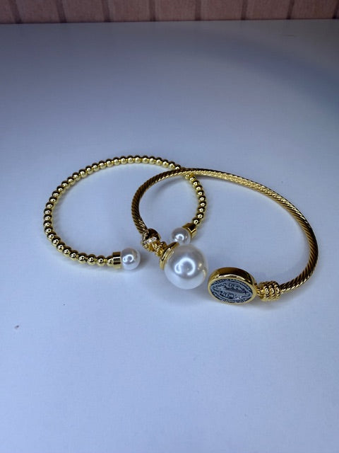 Two Gold rope style bracelets with pearl charms on a light gray background