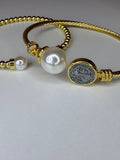 Two Gold rope style bracelets with pearls and a coin charm on a light gray background