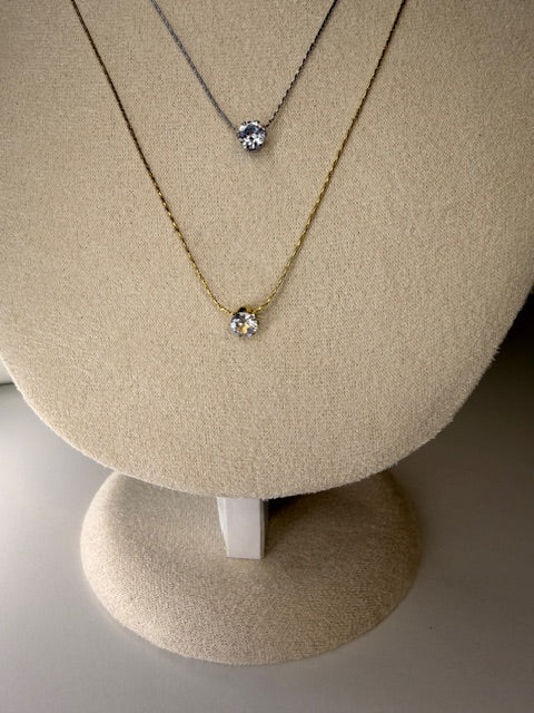 a gold and silver necklace with a stone center on a beige display stand