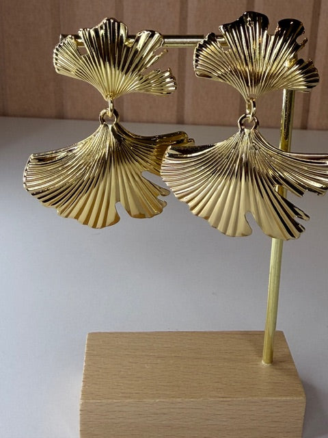 Gold leaf-shaped earrings on a wooden stand against a neutral background