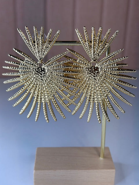 Gold sunburst earrings on a stand against a neutral background