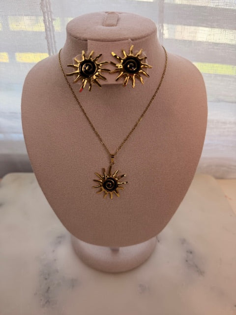 Black and Gold sun-shaped earrings and matching necklace on a pink mannequin bust with a blurred background