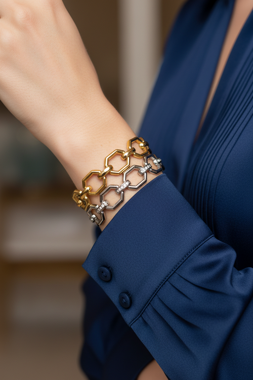 A close-up of a person's wrist wearing a double-layered honeycomb bracelet in yellow gold and silver, paired with a navy blue pleated blouse.