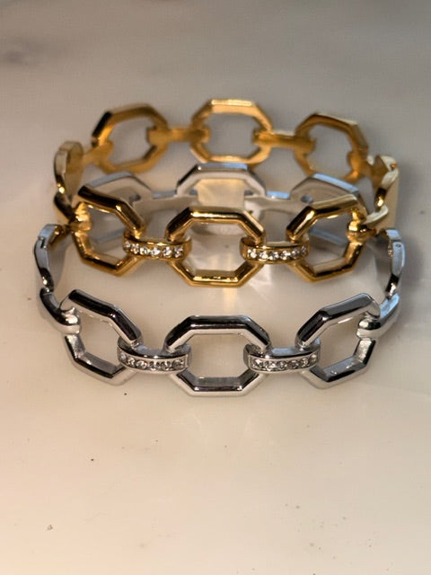 Two chain-link bracelets, one gold and one silver, on a light background.