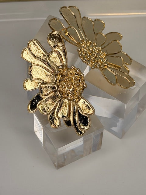 Gold floral earrings on a clear crystal stand against a neutral background