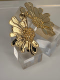 Gold floral earrings on a clear crystal stand against a neutral background