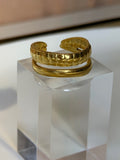 Gold double strand ring on a clear crystal stand with a white background