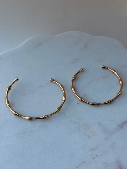 Gold open and adjustable bamboo style bangles on a marble surface