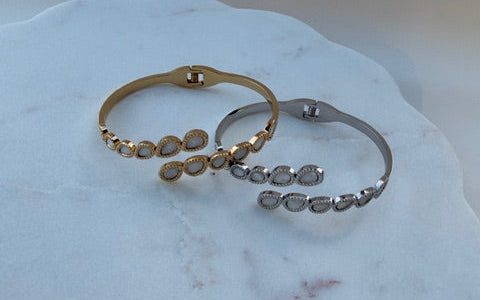 Two gold and silver bracelets on a marble surface