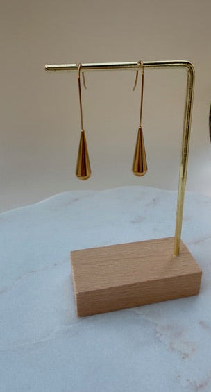 Gold teardrop earrings on a wooden stand with a beige background