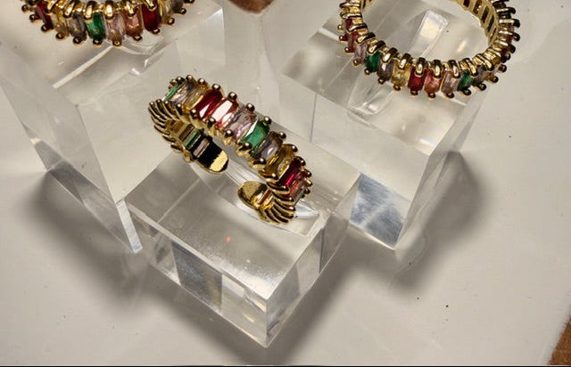 Gold and multicolored gemstone open rings on a clear stand with a dark background