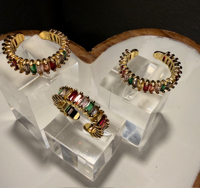 Gold and multicolored gemstone open rings on a clear stand with a dark background