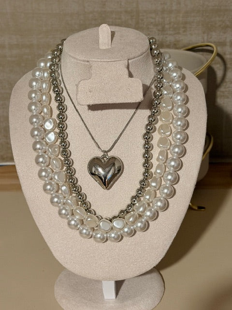 Pearl necklace with a silver heart pendant on a beige stand.