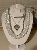 Pearl necklace with a silver heart pendant on a beige stand.