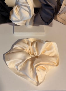 Two beige satin hair scrunchies on a light gray background