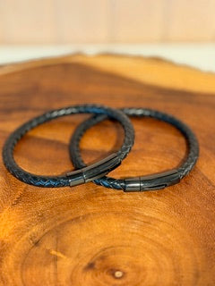 Two black leather bracelets on a wooden surface