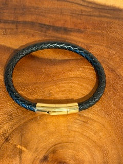 Black braided leather bracelet with a gold clasp on a wooden surface