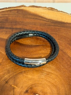 Black leather bracelet with silver clasp on a wooden surface