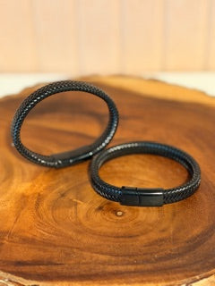 Two black leather bracelets on a wooden surface
