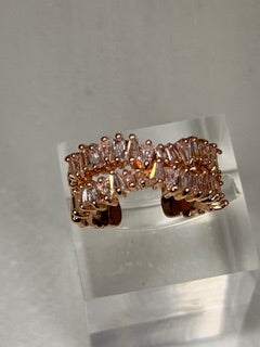 Rose gold ring with clear stones on a clear stand against a light gray background