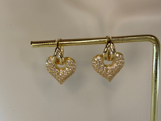 Heart-shaped gold earrings on a stand with a neutral background