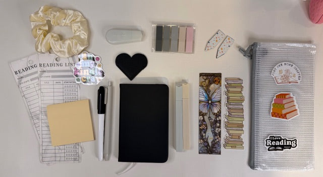 Collection of stationery items including a notebook, pens, and decorative elements on a white surface.