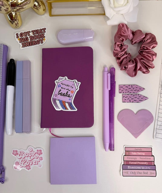 Purple stationery items including a notebook, pens, and stickers on a white surface.