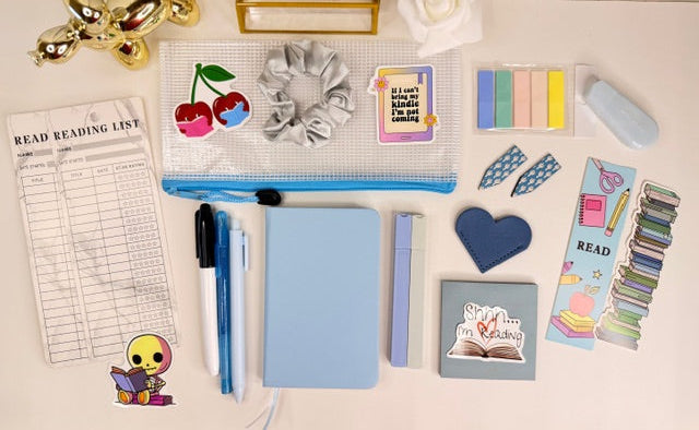 Collection of stationery items including a notebook, pens, and decorative stickers on a light surface.