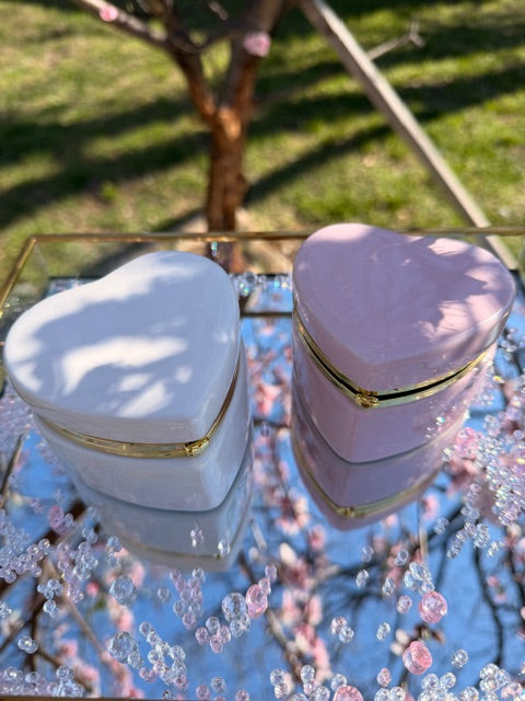 Heart-shaped pink and white containers with gold accents against a blurred natural background