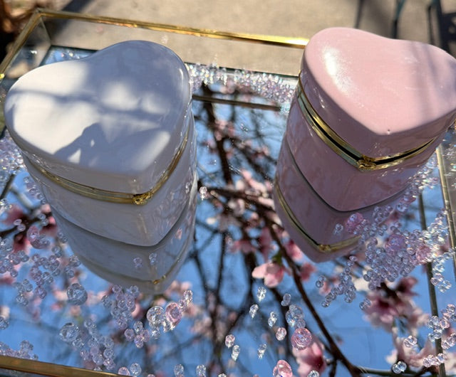 Two heart-shaped boxes, one white and one pink, on a reflective surface with floral background.