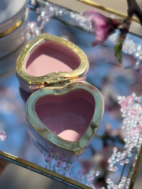 Heart-shaped box open with gold frame on a reflective surface with floral background